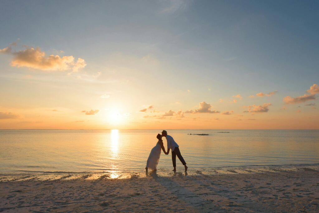 A couple kisses on a tropical beach at sunset in the Maldives, showcasing love and serenity.